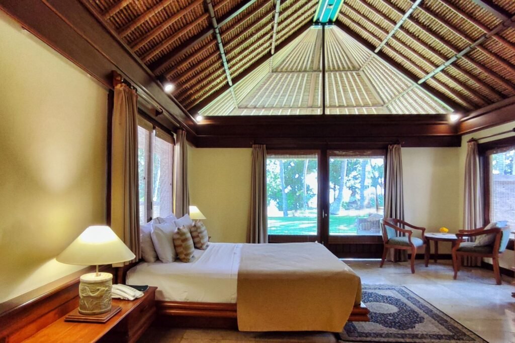 "Cozy seating area inside Deluxe Ocean Villa with sofa and wooden chairs near a large window."