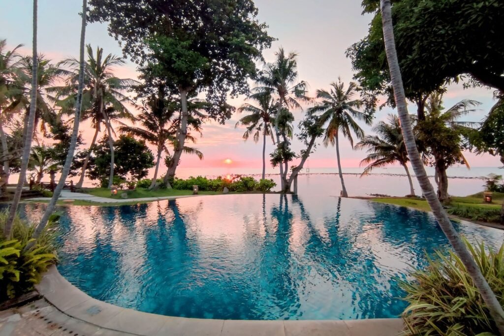 Infinity pool overlooking the ocean at sunset with palm tree reflections