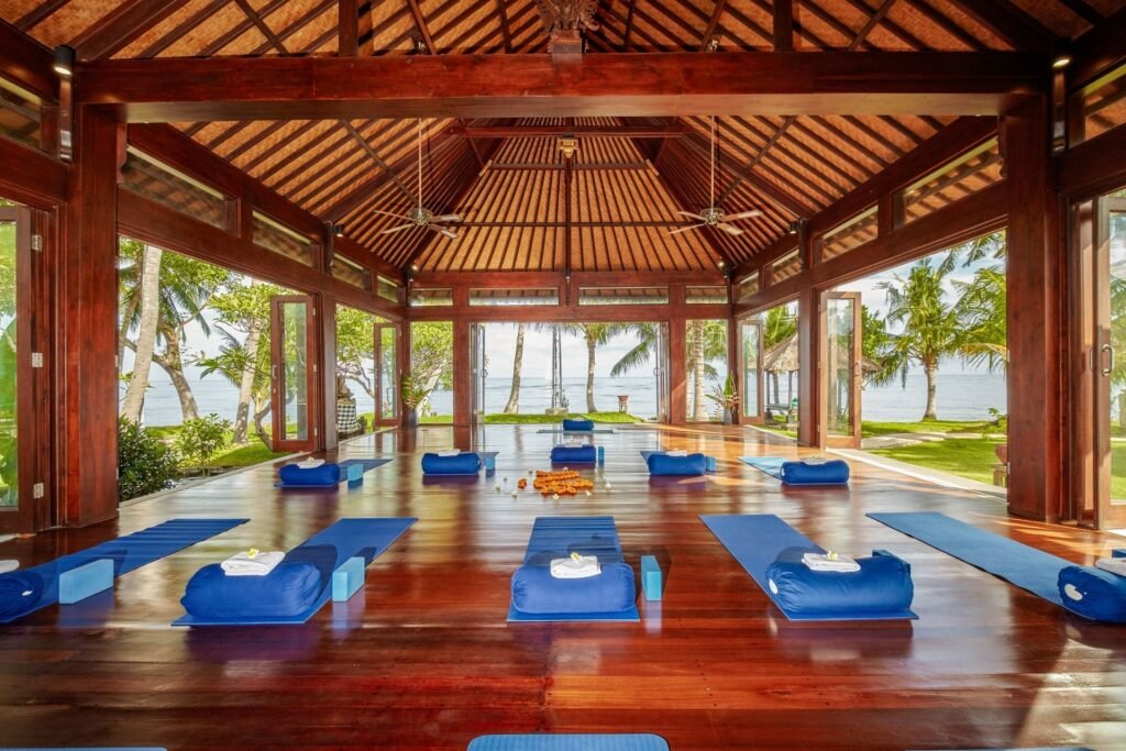 Yoga or meditation room with wooden floors and blue mats, open sides showing greenery outside