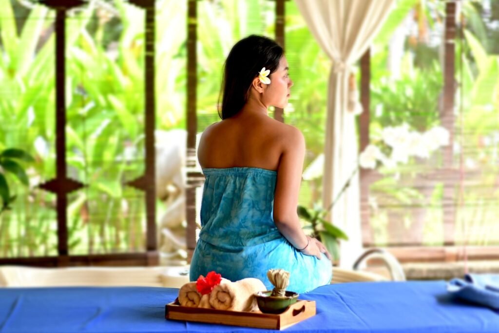 Woman sitting on a spa bed wrapped in a towel, surrounded by a tropical outdoor setting